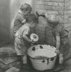 876522 Afbeelding van peuters uit de kindercrêche, die rond een teil met water aan het spelen zijn, op de binnenplaats ...
